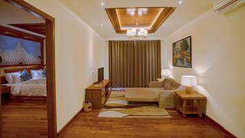 A hotel room with a wooden ceiling, a bed, a sofa, a desk, a TV, and a painting on the wall.
