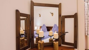 Un espejo con marcos de madera, velas sobre soportes y una cama con ropa de cama a cuadros y una decoración de cabeza de ciervo.