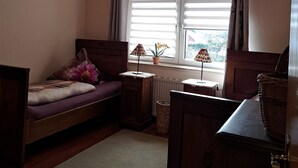 A bedroom with a single bed, a bedside table, a lamp, a potted plant, and a window with curtains. - Vacation apartment for up to 8 people, 140 sqm, 2 WCs, directly on the L.Heide nature reserve (Bispingen)