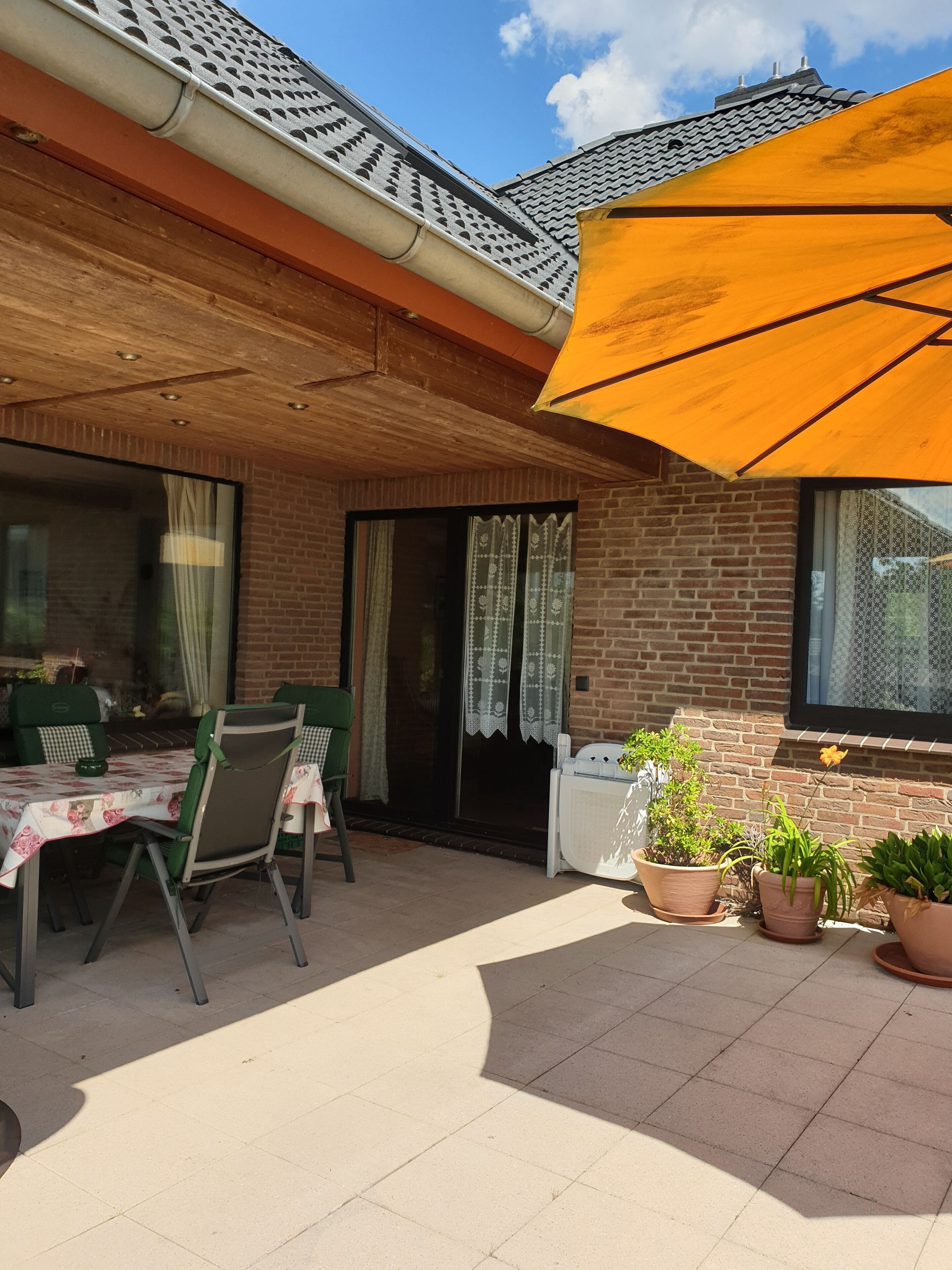 Un patio al aire libre con una mesa, sillas, plantas en macetas y un paraguas grande.