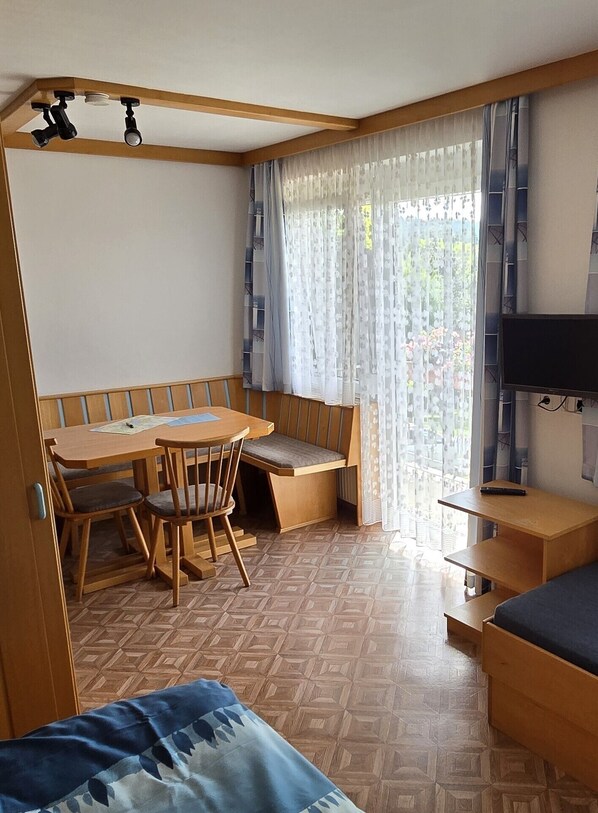 A compact room with a wooden dining table and chairs, a bench, a bed, and a TV.