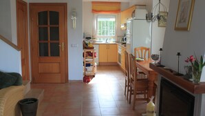 A spacious living area with a fireplace, a dining table, and a kitchen in the background. - Family-friendly bungalow complex with a lot of green and a large pool (Miami Playa)