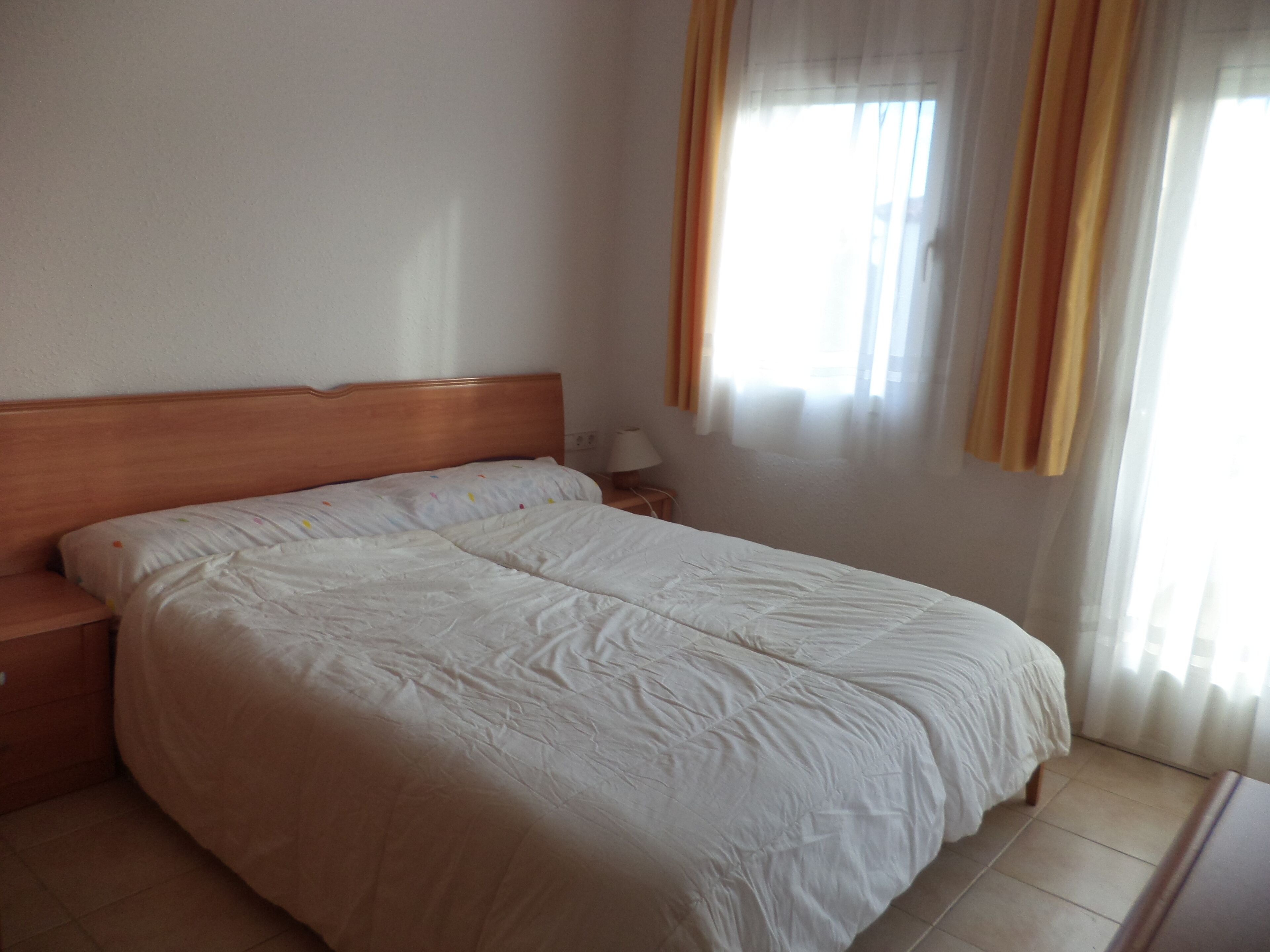 Hotelkamer met een groot bed, een houten hoofdeinde, een nachtkastje, een lamp en een raam met gordijnen.