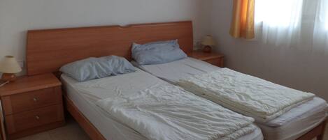 Ein Doppelbett mit hölzernem Kopfteil, zwei Nachttische mit Lampen und ein Fenster mit Vorhängen.