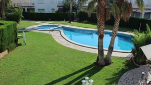 A swimming pool with a curved design, surrounded by well-maintained grass and palm trees. - Family-friendly bungalow complex with a lot of green and a large pool (Miami Playa)