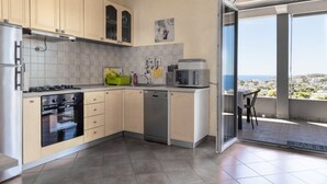 Una cucina moderna con mobili color beige, lavastoviglie, fornello e microonde. Una finestra offre vista sulla città.