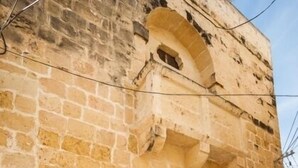 Un edificio de piedra con puerta de madera y ventana con reja metálica.