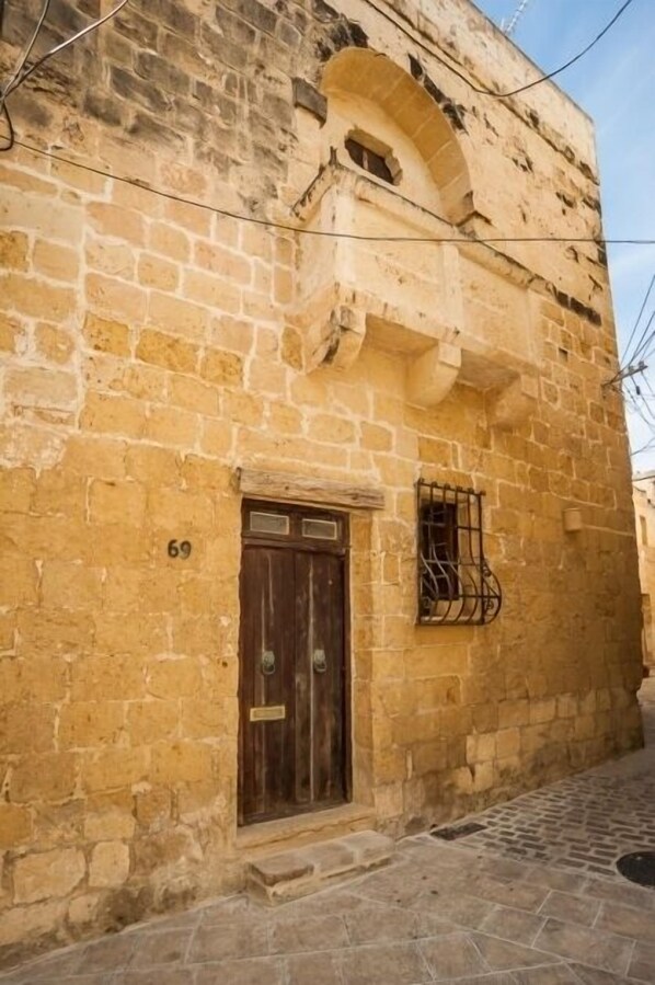 A stone building with a wooden door and a window with a metal grille.