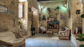 Una habitación rústica con paredes de piedra, muebles de mimbre, un cuadro y una mesita.