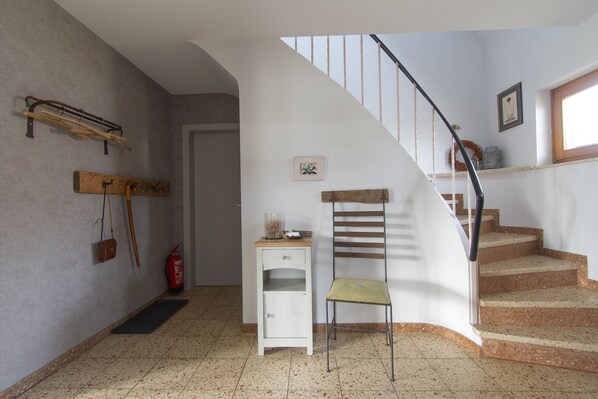 Una escalera con barandilla de madera y pared blanca, con un extintor y un estante pequeño.
