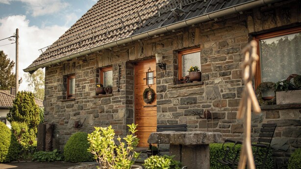Una casa de piedra con puerta de madera, plantas en macetas y un banco.