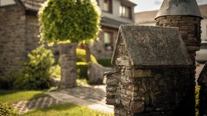 Una estructura de piedra con techo puntiagudo, posiblemente un monumento o hito histórico, en un patio con un edificio de ladrillo al fondo.