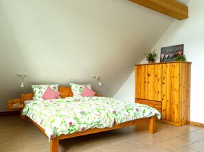 A bedroom with a sloped ceiling, a wooden bed with floral bedding, a wooden wardrobe, and a wall-mounted light fixture.