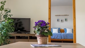 Une chambre avec un lit, une télévision et une plante en pot ornée de fleurs violettes.