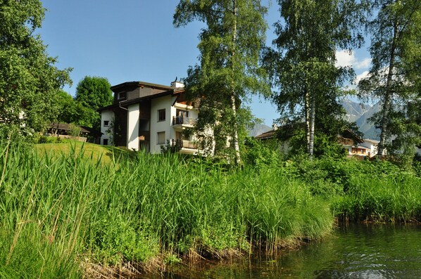 A house with a balcony, surrounded by lush greenery and a body of water.