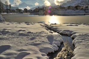 A snow-covered landscape with a frozen lake, buildings in the background, and a church.