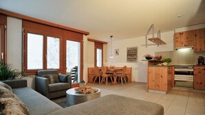Una sala de estar moderna con un sofá, una mesa de comedor con sillas, y una cocina con armarios de madera y electrodomésticos.