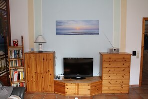 Ein Wohnzimmer mit einem Holzschrank, einem Fernseher und einem Sonnenuntergangsbild.