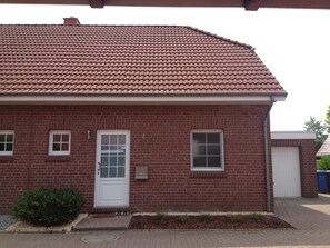 Ein Gebäude aus roten Ziegeln mit einem Ziegeldach, einer weißen Tür und zwei Fenstern.
