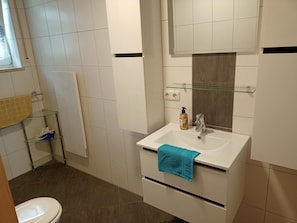 Une salle de bain avec un lavabo blanc, un miroir, un porte-serviettes et une étagère en verre.