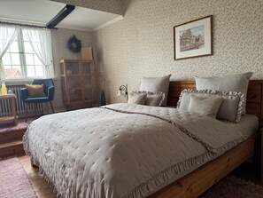 Une chambre à coucher avec un grand lit, une tête de lit en bois, un tableau encadré au mur et une fenêtre avec des rideaux.