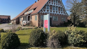 A traditional half-timbered building with a steeply pitched roof, a prominent entrance with a door, and a signboard. - FeWo Elblust - Altländer Obsthof (Hollern-Twielenfleth)