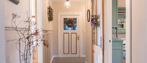 A hallway with a door, a hanging light fixture, a rug, and a vase with branches.