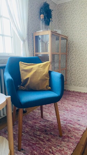 Een blauwe fauteuil met een geel kussen, een houten kast en een kamerbreed tapijt met een patroon.