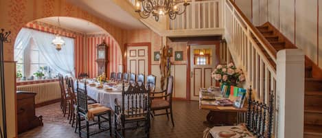 Comedor con una gran mesa, sillas, un candelabro y una escalera.