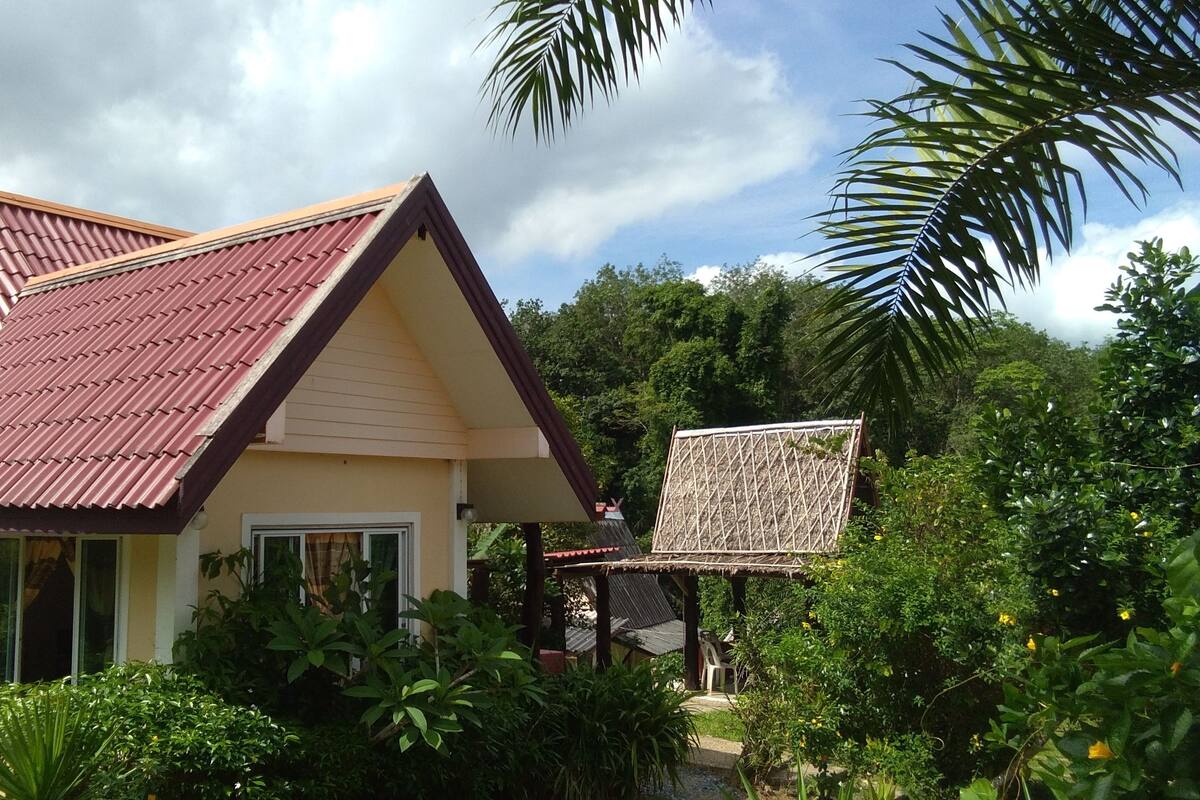 A house with a red-tiled roof, surrounded by lush greenery and a clear sky.