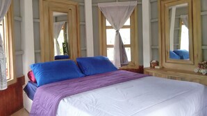 Une chambre à coucher avec un grand lit, deux tables de chevet, un miroir et une fenêtre avec un rideau.