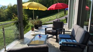 Une terrasse avec des meubles d’extérieur, deux parasols et une vue sur la végétation environnante.