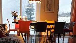 Un salon moderne doté d’une grande fenêtre, d’un coin repas avec des chaises, d’un canapé et d’une table décorée de bougies.