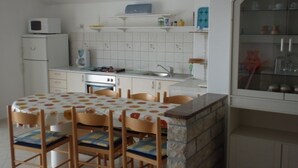 A compact kitchen with a dining table, chairs, a microwave, a stove, and a cabinet with shelves. - Apartment in Kukljica with Seaview, Terrace, Air condition, WIFI (4567-3) (Kukljica)