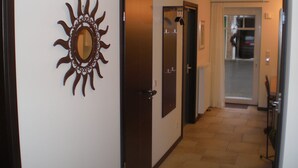 En hall med en spegel formad som en sol, en dörr och en utsikt in i ett rum där man kan se en bil genom ett fönster.