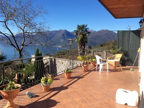 A terrace with potted plants, a white chair, and a view of mountains and a lake.