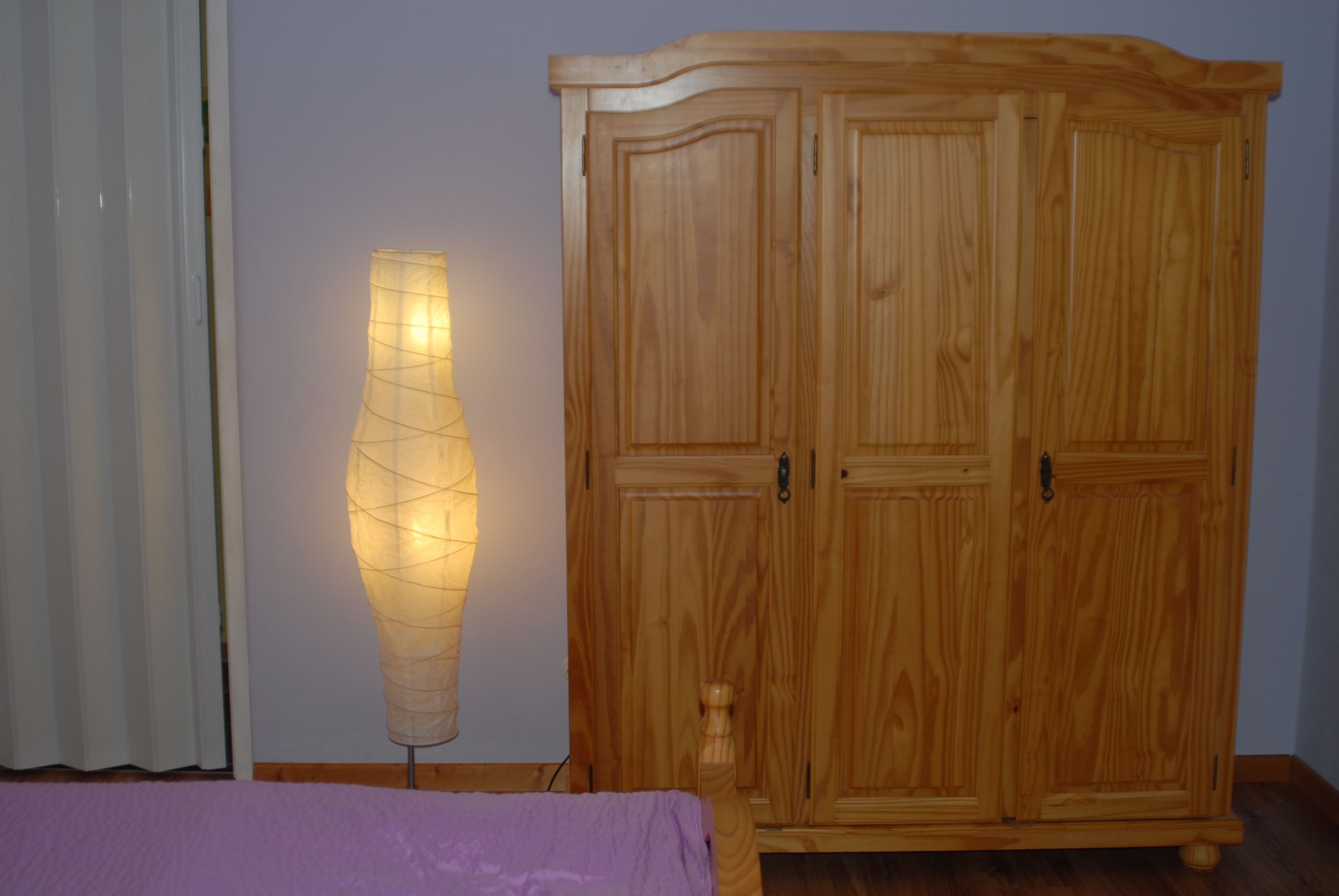 A wooden wardrobe with two doors and a standing lamp beside it.