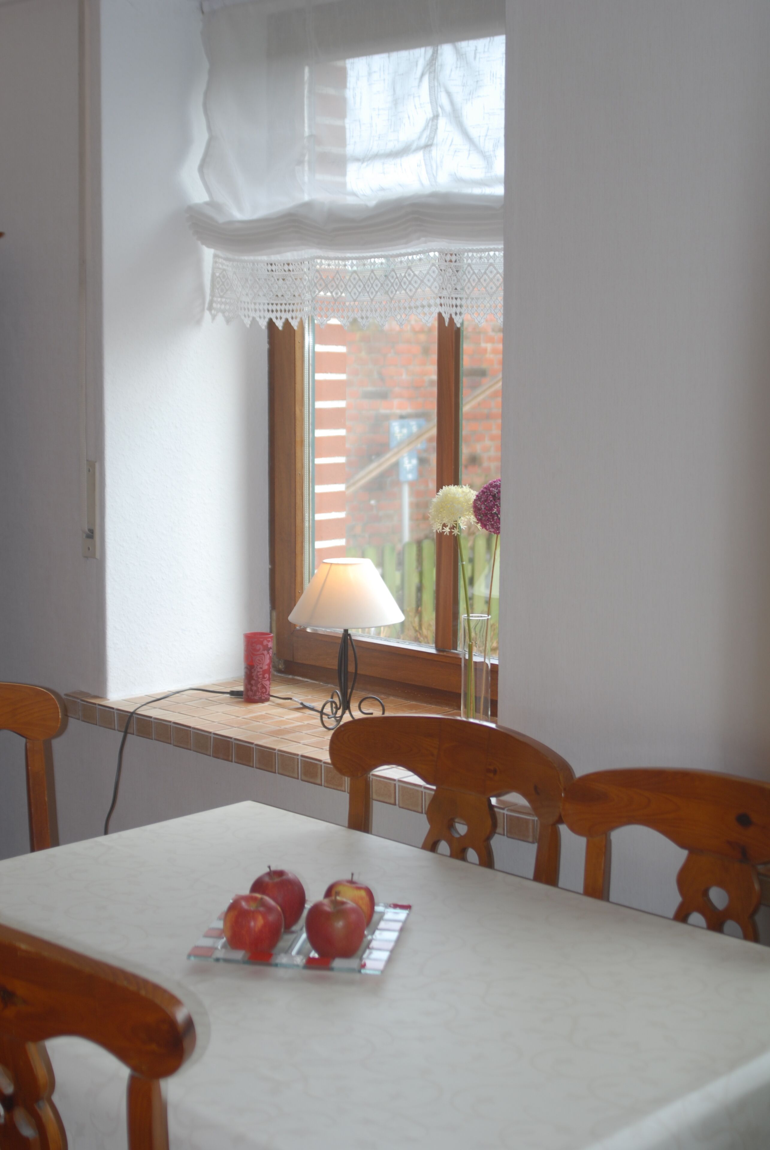 Ein Essbereich mit einem Tisch für vier Personen, einem Fenster mit Spitzenvorhängen und einer Lampe auf der Fensterbank.