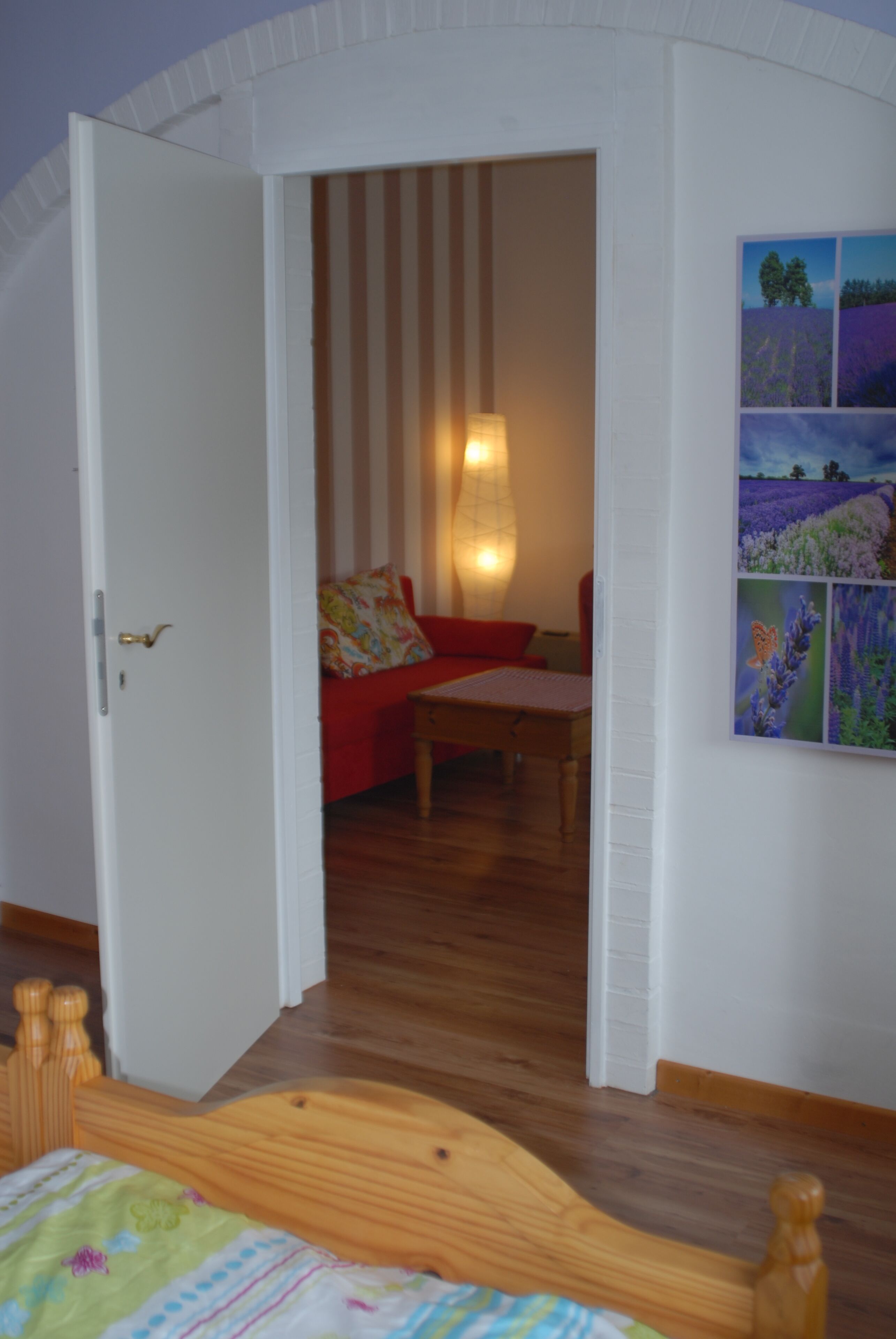 Ein Zimmer mit einem hölzernen Bett, einem roten Sofa, einem Holztisch und einer Wandleuchte.
