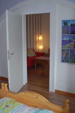 Een kamer met een houten bed, een rode bank, een houten tafel en een wandlamp.