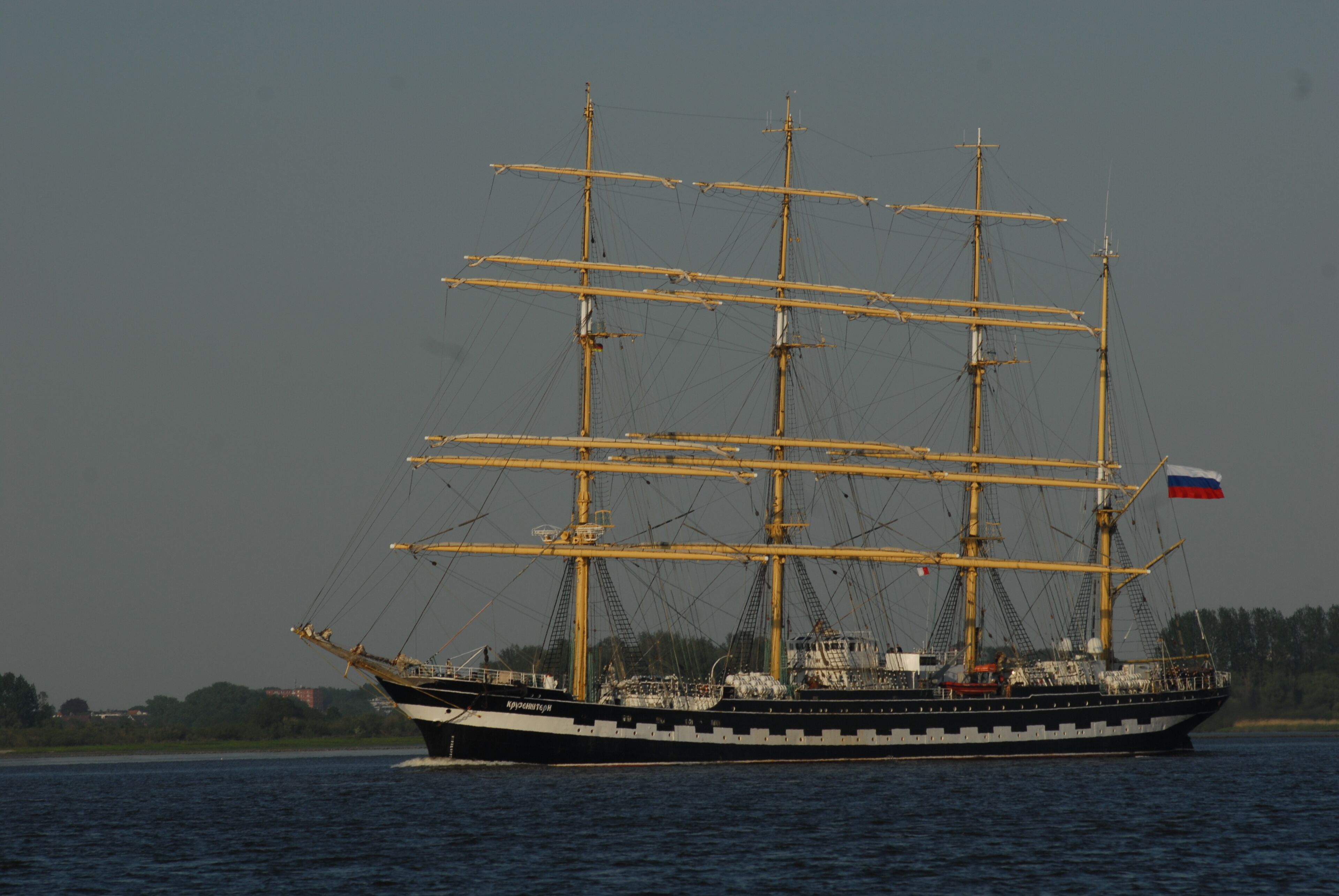 A large, three-masted sailing ship with a Russian flag, sailing on a body of water.