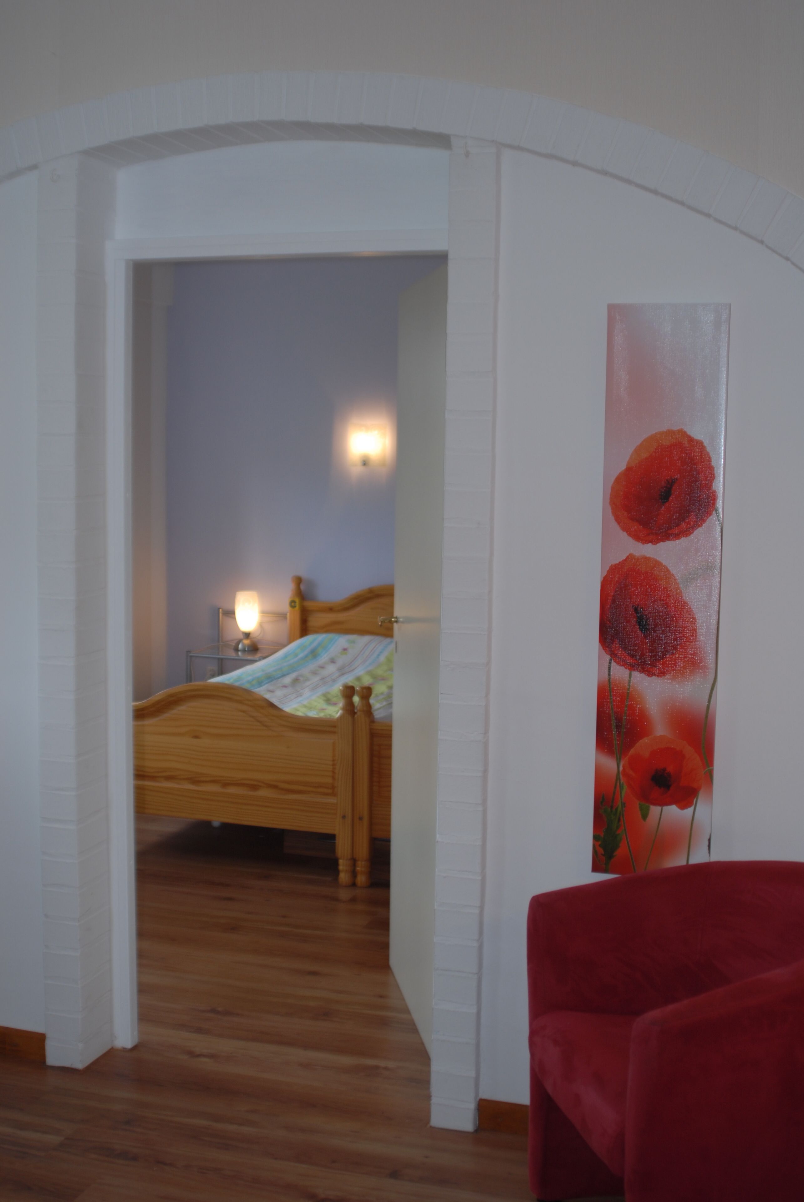 Ein Schlafzimmer mit einem hölzernen Bett, einem roten Sessel und einem Gemälde von roten Blumen an der Wand.