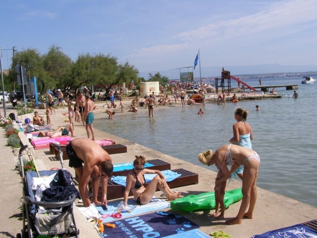 A crowded beach with people sunbathing and swimming.