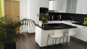 Una cocina moderna con armarios blancos, encimera negra y dos taburetes blancos.