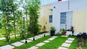 A well-maintained garden with a paved pathway, various potted plants, and a building with a white exterior and large windows. - Michelles House (Playa del Carmen)