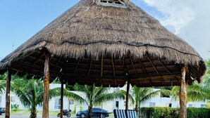 A thatched-roof pavilion with benches and a tiled floor, surrounded by palm trees. - Michelles House (Playa del Carmen)