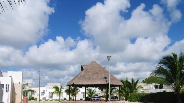 A swimming pool with a thatched-roof pavilion, palm trees, and a clear blue sky. - Michelles House (Playa del Carmen)