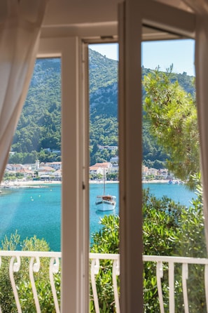 Un balcon offrant une vue sur une ville cĂŽtiĂšre, un bateau sur lâeau et, en arriĂšre-plan, des montagnes.