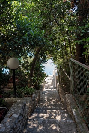 Un chemin de pierres qui monte une pente, bordé de verdure et délimité par une clÎture en métal.
