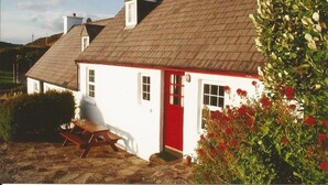 Una casa blanca con puerta roja, un patio de piedra y un jardín con flores rojas.